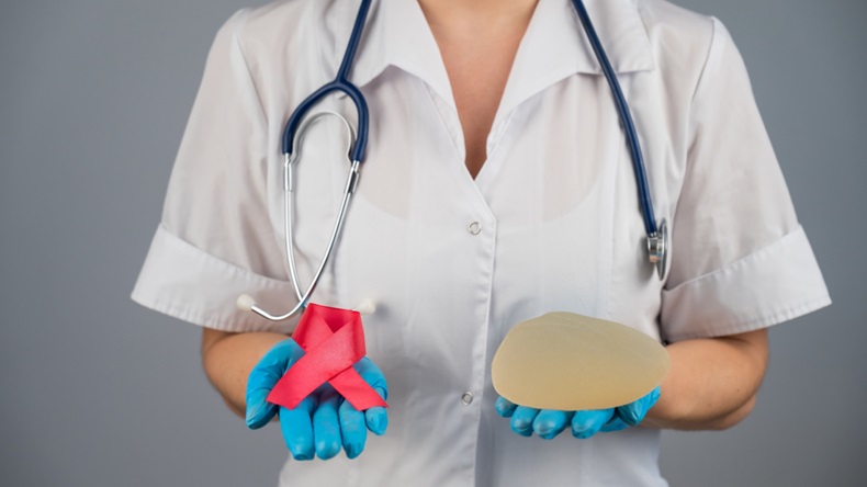 Doctor holding a silicone breast implant and a pink ribbon.
