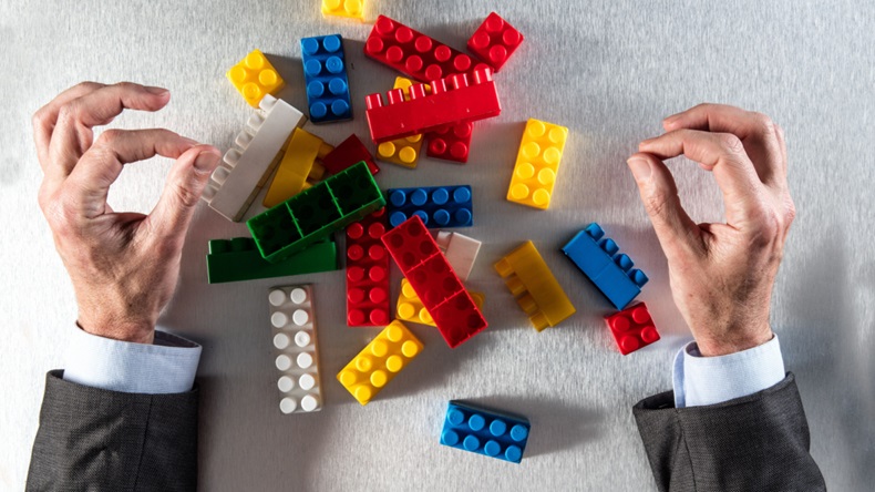 Concept of reorganization or restructuring with businessmans hands facing a group of messy plastic blocks on his desk