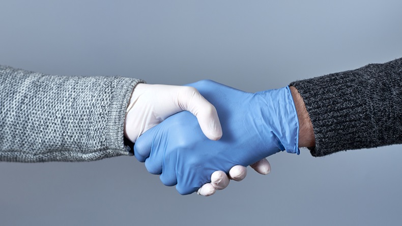 The concept of a safe handshake. Shaking hands in medical gloves on gray background