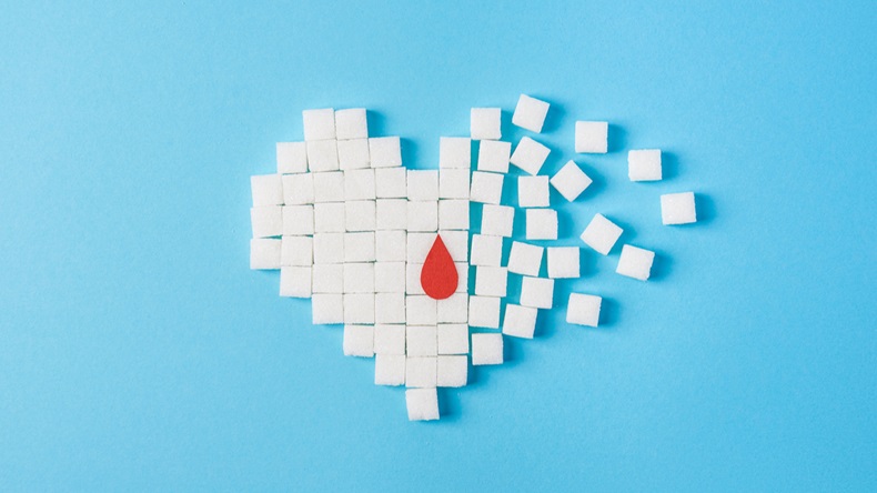 the drop of blood on broken heart made of pure white cubes of sugar isolated on blue background