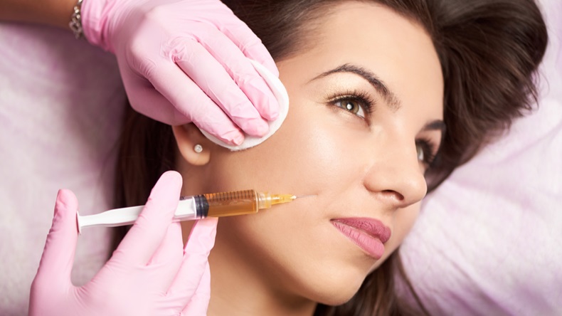 Close-up of a woman getting injected in the face with a dermal filler by a doctor in medical gloves.