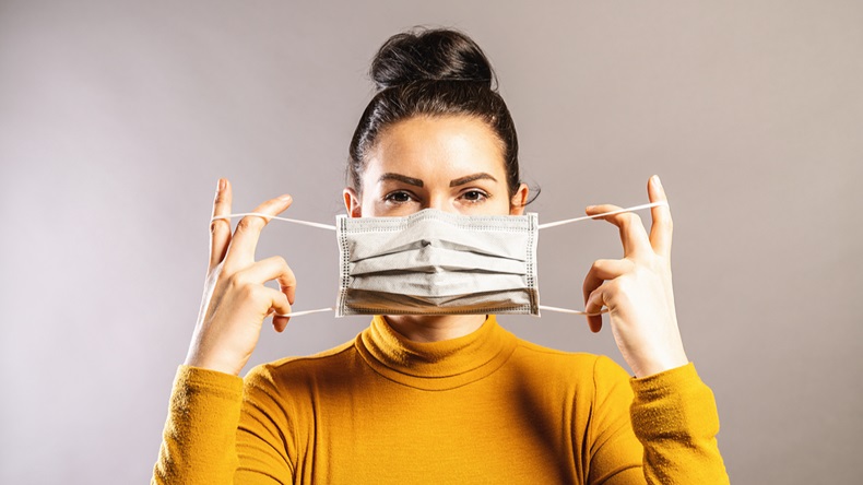 Woman holding disposable paper mask over lower half of face