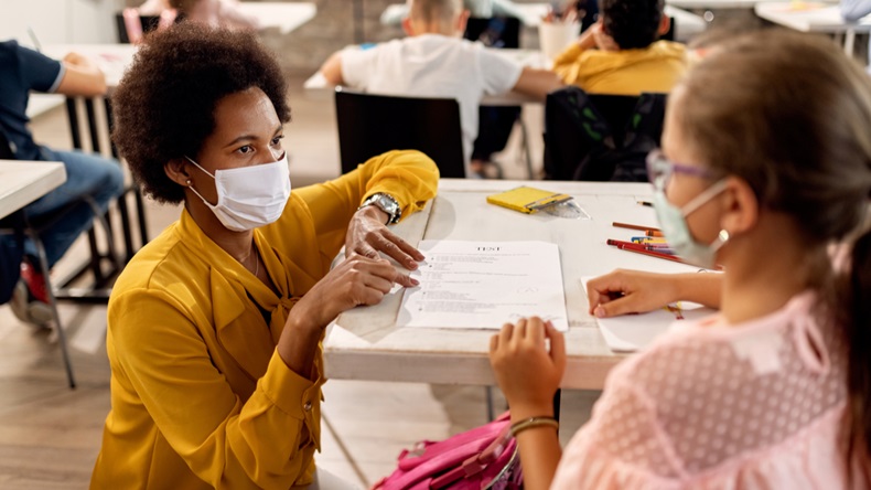 A teacher and schoolgirl wearing protective face masks while discussing test results at school.
