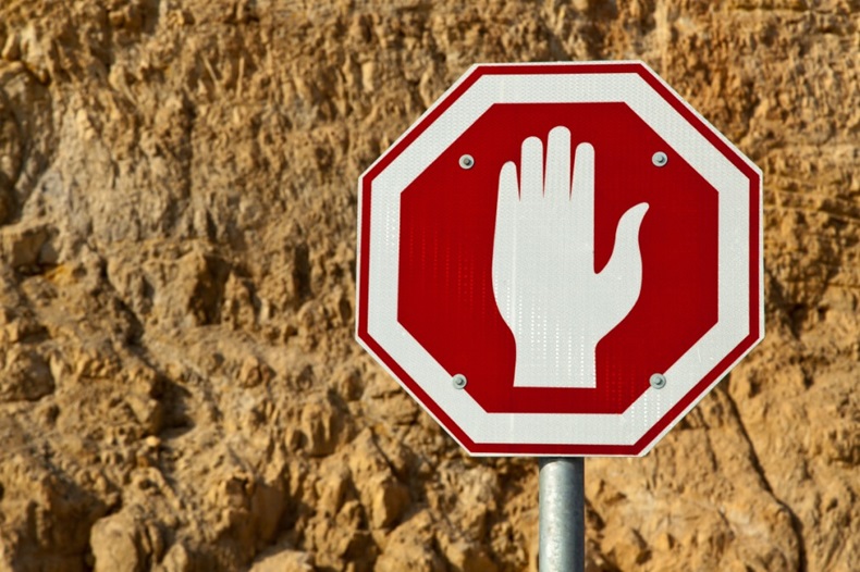 Hand making "stop" gesture on a red sign against a rocky background.