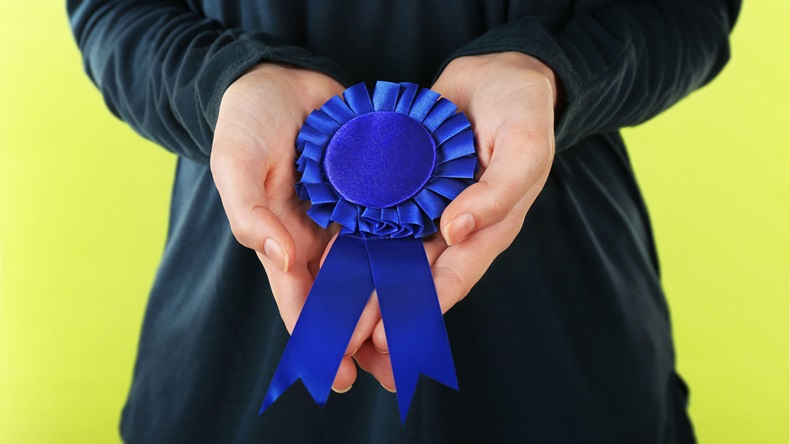 Woman holding blue award prize ribbon.