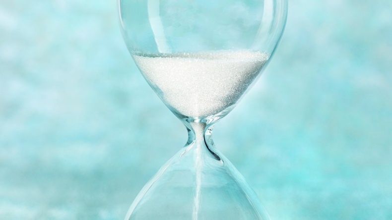 A close-up of a sand clock on a teal blue background.