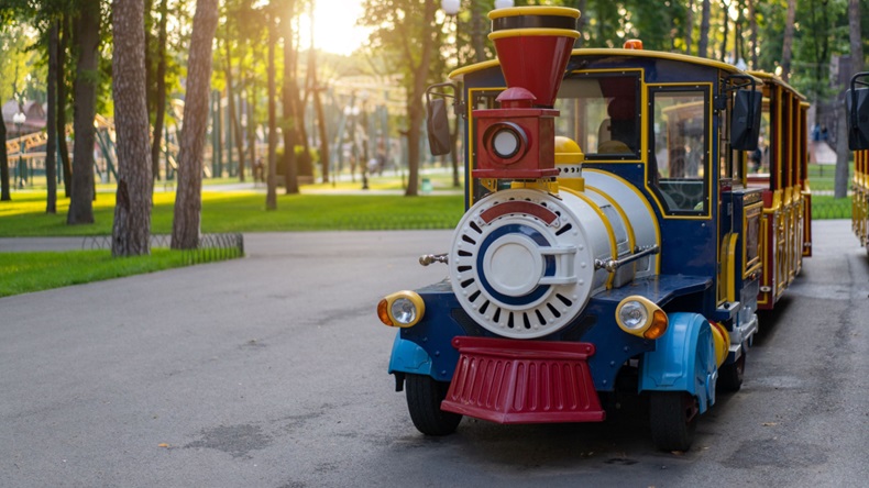 A small train ride for children stands in a parking lot.