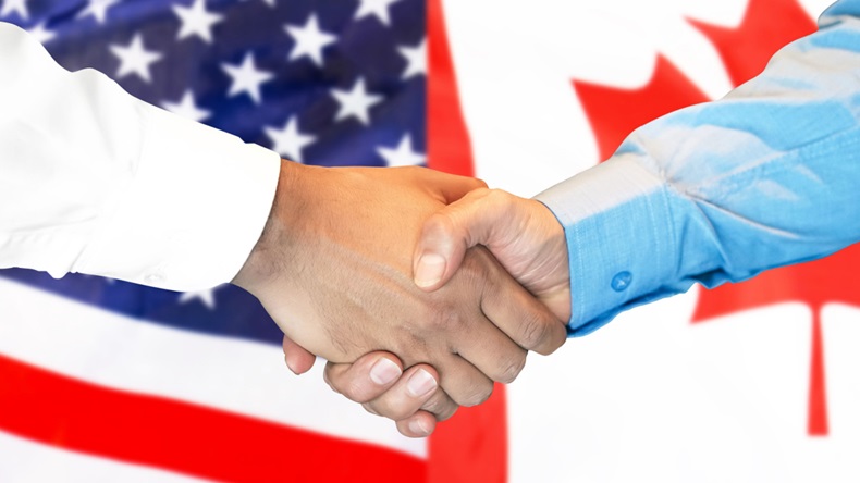  Men shake hands against the background of the Canada and US flags. 