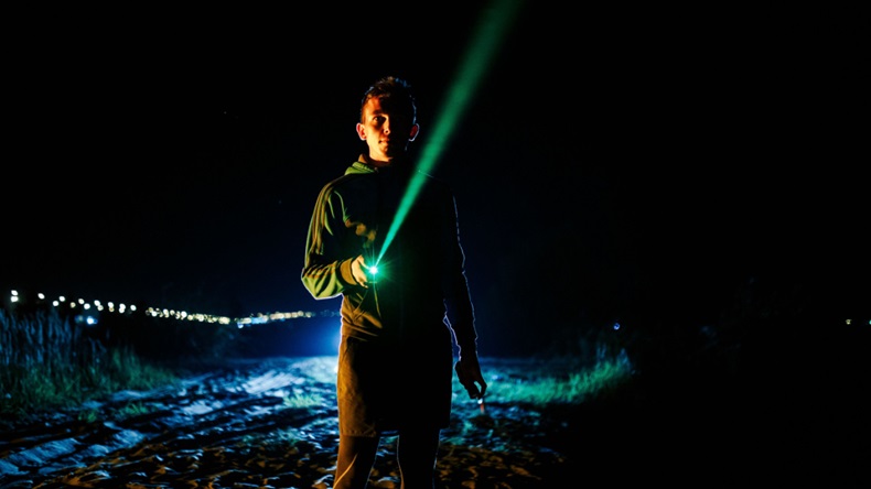 Nighttime outside scene of a young teenager aiming a green laser pointer at the sky.