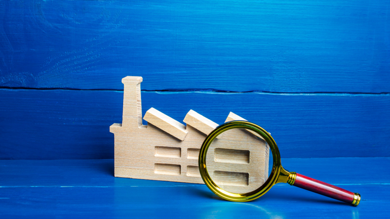 wooden factory with magnifying glass on blue background