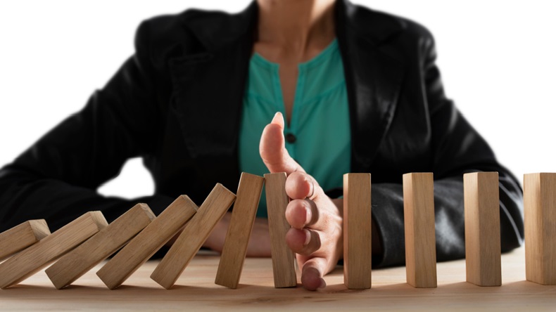 Businesswoman using her hand to prevent dominos from falling, representing the concept of risk management.