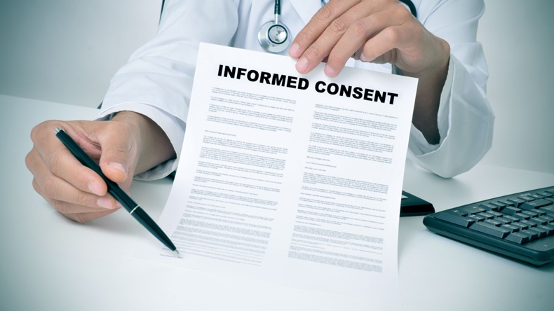 A doctor in his office showing an informed consent document and pointing to the signature line.