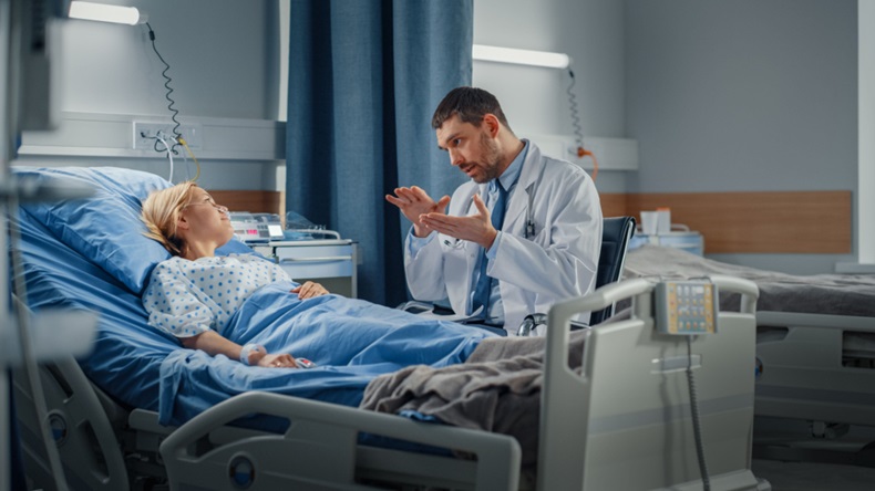 A doctor consults a woman awaiting srugery in a hospital bed.