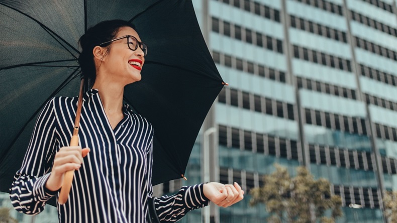 Smiling businesswoman standing under umbrella.