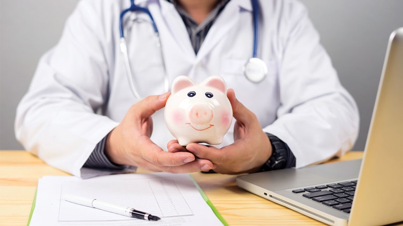 Doctor holding out your piggy bank wanting payment/ Your Savings To Pay Bill, insert coins to it,Stethoscope financial checkup or saving for medical insurance costs money plan fee Lifestyle concept 
